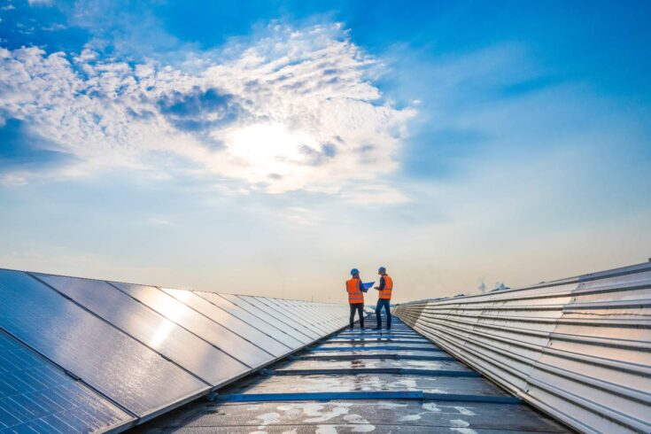 Two technicians in distance discussing between long rows of photovoltaic panels.