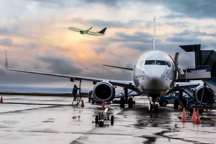 Passenger airplane being refueled and loaded with cargo before the flight near the terminal in an airport at the sunset.