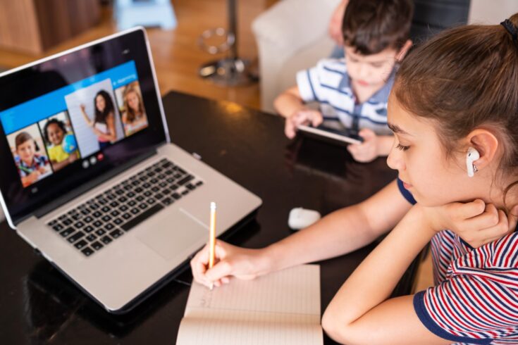 Two young children homeschooling and distance learning using a laptop and video conferencing