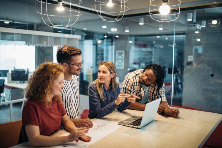 Successful group of business people and designers at work in office around a table and laptop