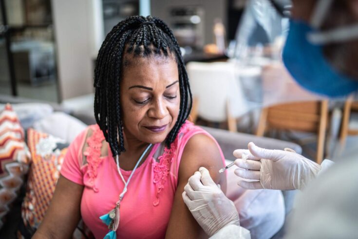 Doctor applying vaccine in a mature woman at home