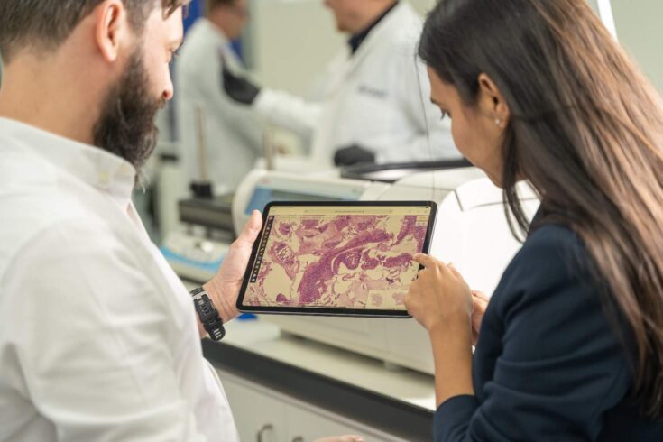Two people looking at a smart tablet with an image of cancer cells