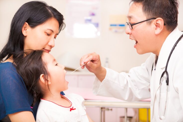 Pediatrician checking little girl throat in clinic