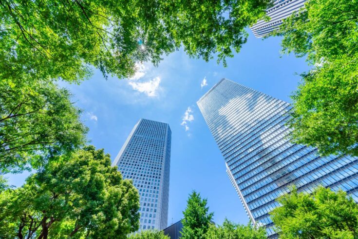 Looking up view of panoramic modern city skyline with blue sky and green tree in Shinjuku, Tokyo, Japan