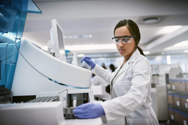 Shot of a young woman wearing safety goggles using a machine to conduct a medical test in a laboratory