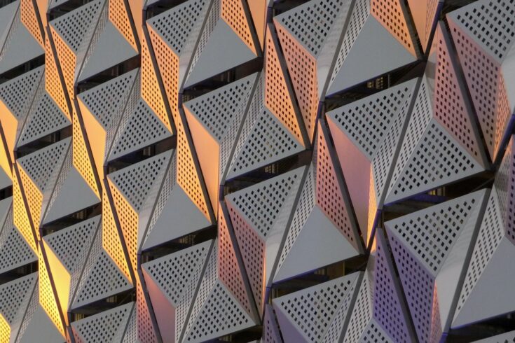 Modern steel cladding with angular geometric patterns and square holes in a shiny metallic finish with colored reflection on the wall of a car park