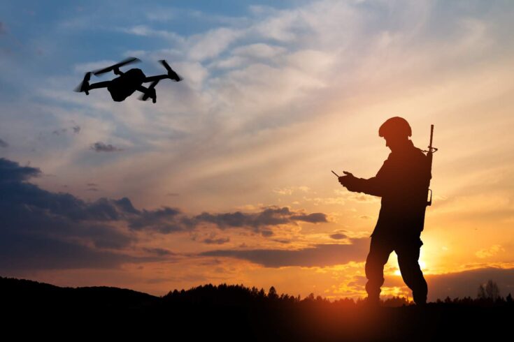 Silhouette of soldier using drone and laptop computer for scouting during military operation.