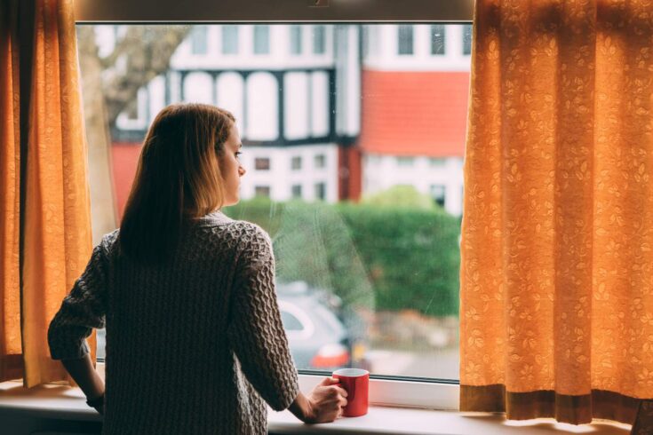 Woman staying home for safety during coronavirus pandemic and observing empty streets