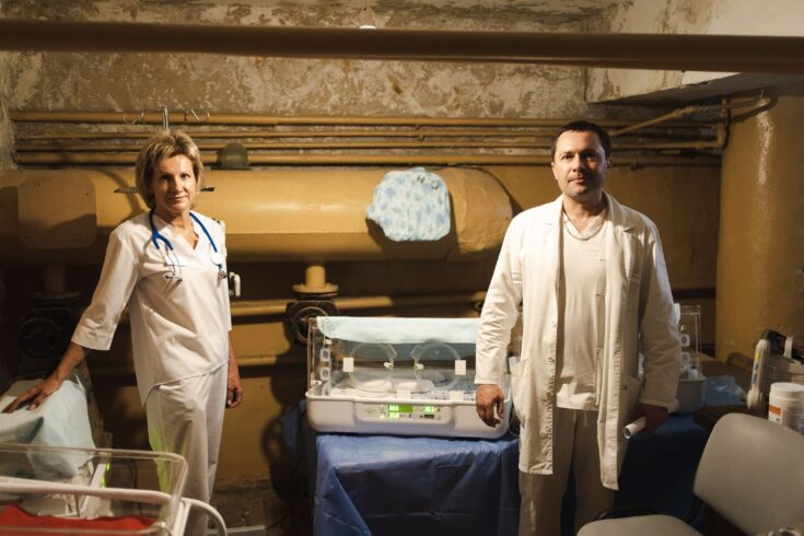 Two doctors stood in a bomb shelter with an incubator on the table between them