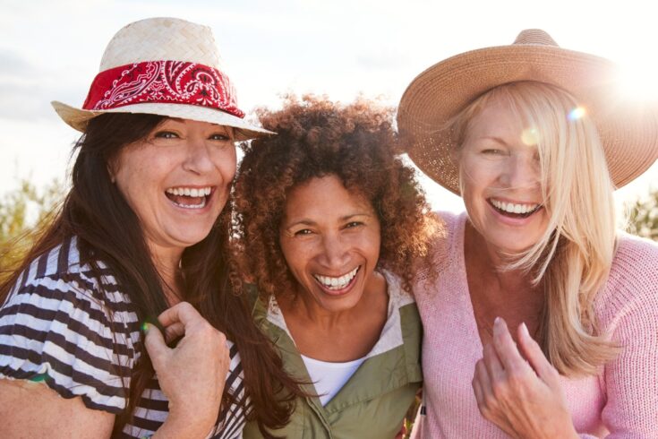Portrait of mature female friends walking through field on camping vacation