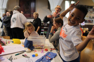 A child, close to the camera, beams with enjoyment as he and other children engage in craft activities.