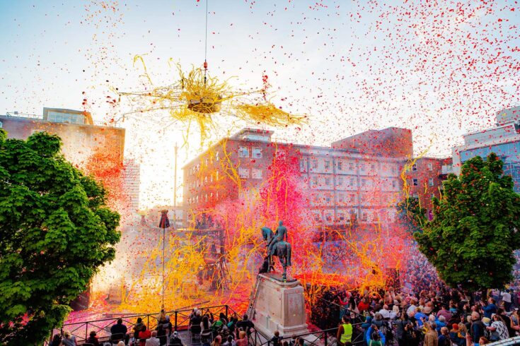 Explosions of pink and yellow erupt above a statue and crowd in Coventry, celebrating the city’s City of Culture status, in 2021.
