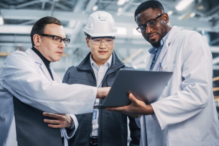 Team of diverse professional heavy industry engineers wearing safety uniform and hard hats working on laptop computer.