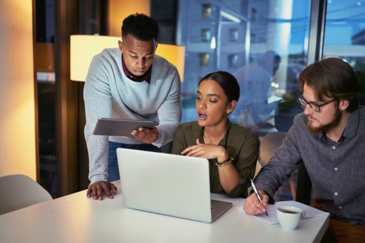 Shot of a group of young businesspeople using a laptop together during a late night at work