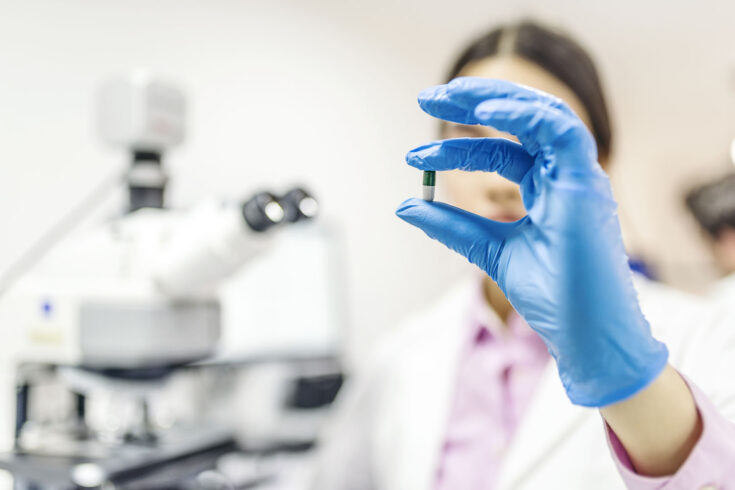 Close up of young female scientist or doctor holding and showing pill in laboratory.