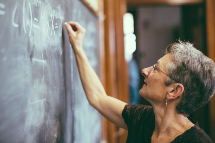 Senior female mathemathics professor writing a formula to the chalkboard