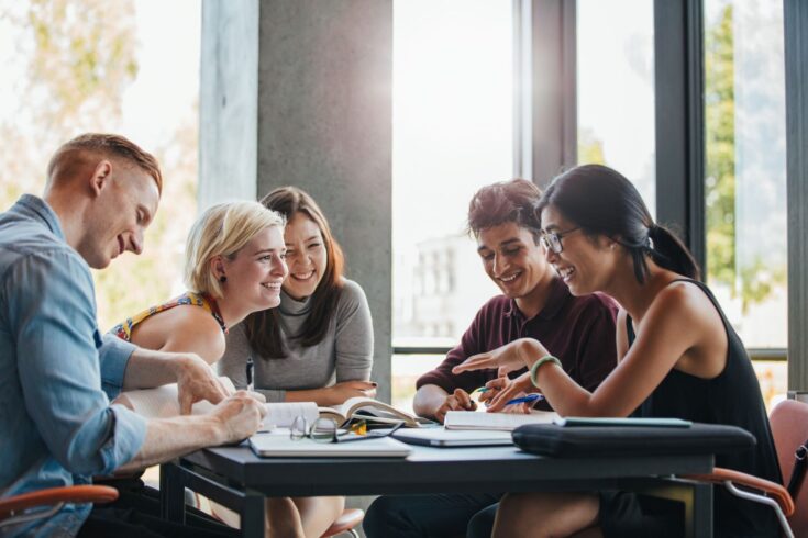 Group of multiracial people around a table, smiling and writing notes.