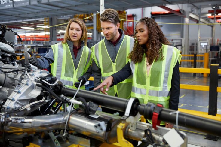 Male and female engineers in reflective clothing discussing over machinery in car plant.