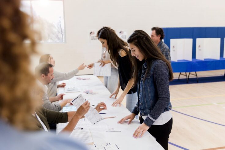 Women stand in a row to sign up to vote while the polling place volunteers help them.
