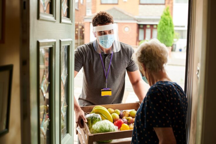 A young volunteer visits an elderly resident with his facemask on delivering fresh produce