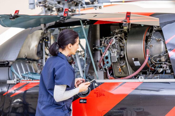 Aircraft mechanic checking helicopter engine, back view. Female worker in blue uniform in airplane hangar, mid shot