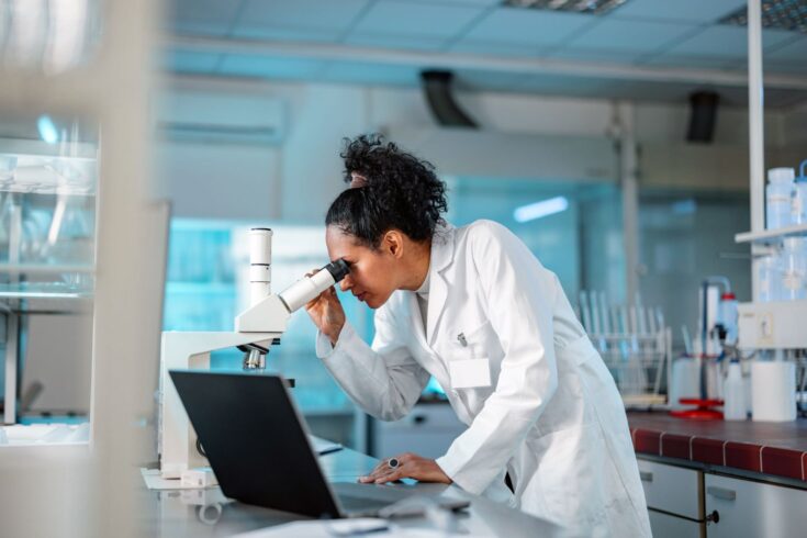 Female scientist looking under a microscope and using a laptop in a laboratory