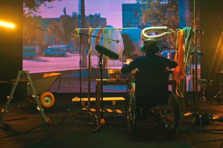 Male on wheelchair imitating various robot sounds against screen with 3D film in studio