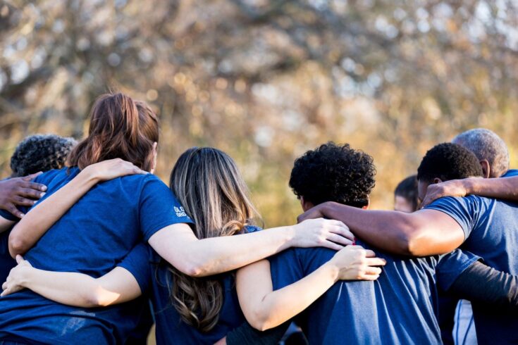 Diverse group of people standing with their arms around one another.