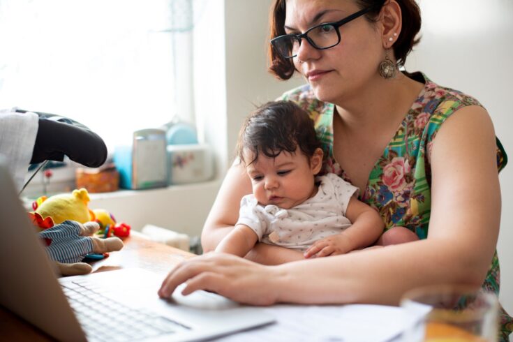 A woman on a laptop with a baby on her lap