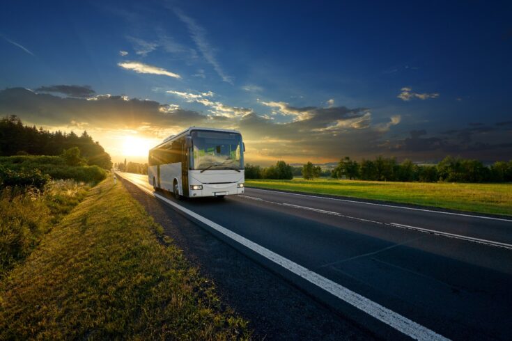 White bus arriving on the asphalt road in rural landscape in the rays of the sunset