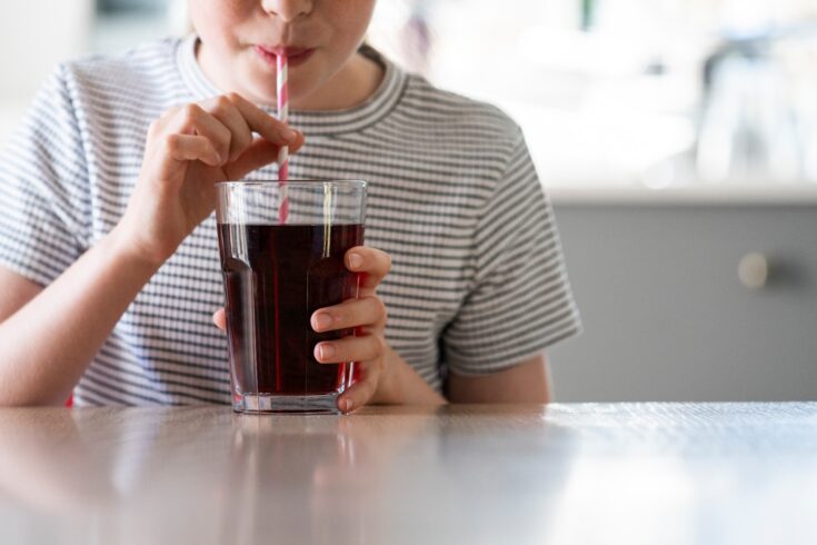 Close up of girl drinking sugary fizzy soda from glass with straw