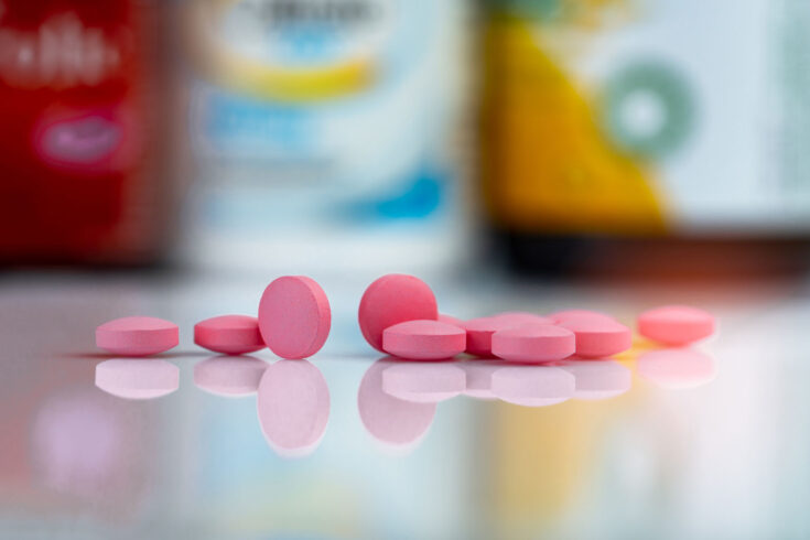 Pink tablets pills on blurred background of drug box and drug bottle.