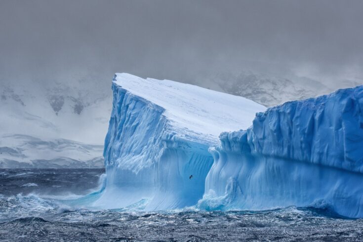 Massive iceberg floating in the Southern Ocean in Antarctica with snow covered mountains in the background