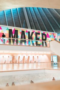 A photograph of a large sign in London’s Design Museum reading “Maker”. In the background you can see visitors in the museum.