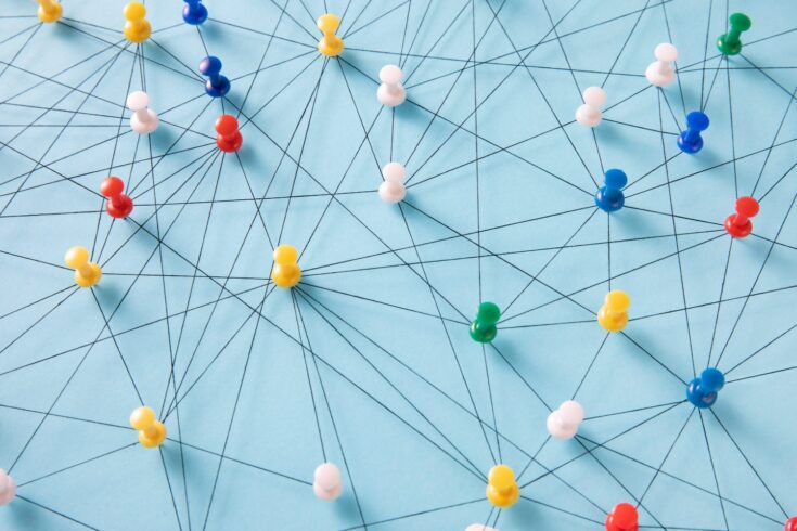 An arrangement of colourful pins linked together with string on a pale blue background suggesting a network of connections.