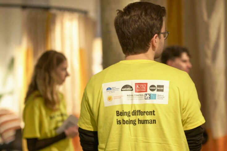 Three people wearing yellow t-shirts with various organisation logos on and text saying 'Being Human is Being Different'