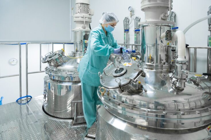 Pharmaceutical factory woman worker in protective clothing operating production line in sterile environment