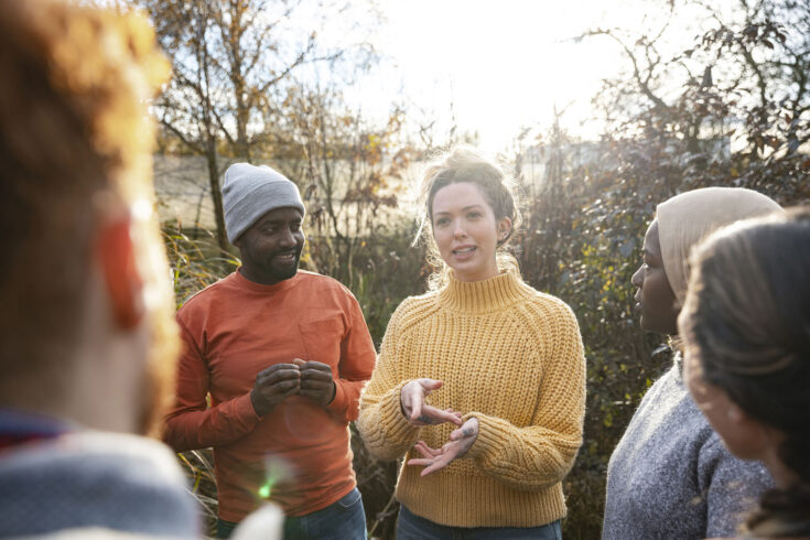 A multiracial group of volunteers wearing warm casual clothing and accessories on a sunny cold winters day. They are talking before they start working on a community farm, planting trees and performing other tasks.