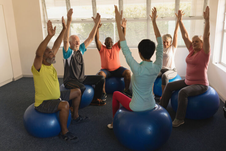 Front view of female training senior people in performing exercise ball at home.