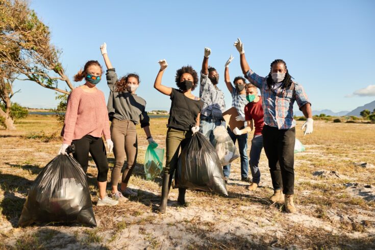 roup of diverse young volunteers wearing face masks cheering together during a community cleanup in a nature reserve
