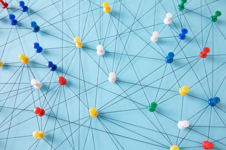 An arrangement of colorful pins linked together with string on a pale blue background suggesting a network of connections