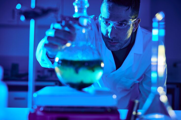 Man looking at beaker in laboratory flooded with blue light