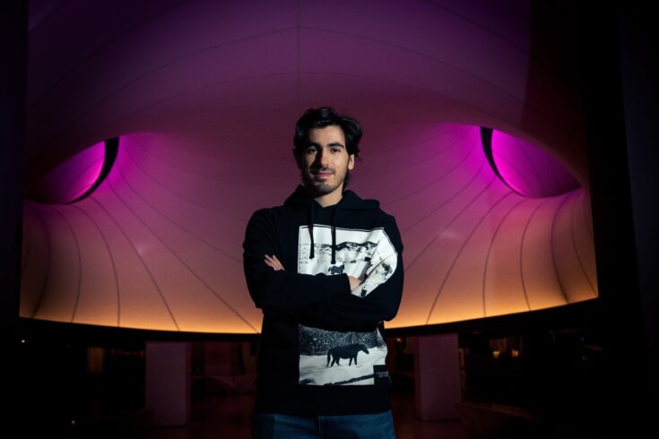 Young man stood against a background lit up pink and orange