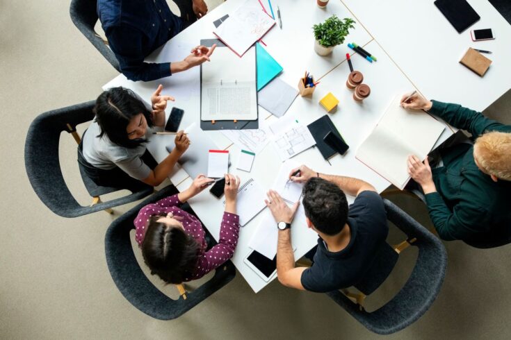 op view shot of business colleagues discussing over a new project in office. Group of young men and woman brainstorming around table while working on new project