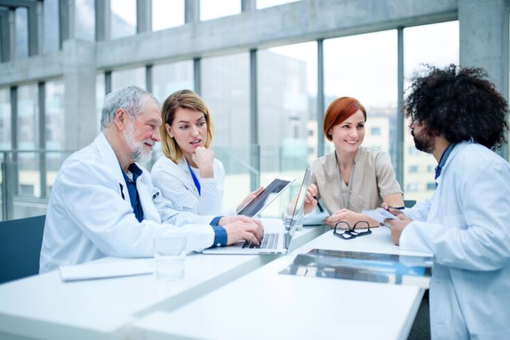 A group of doctors with laptop on conference, medical team discussing issues.