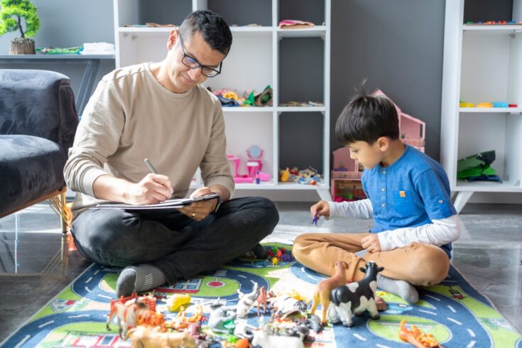 A professional child psychologist observing little boy playing with toys at the psychotherapy session