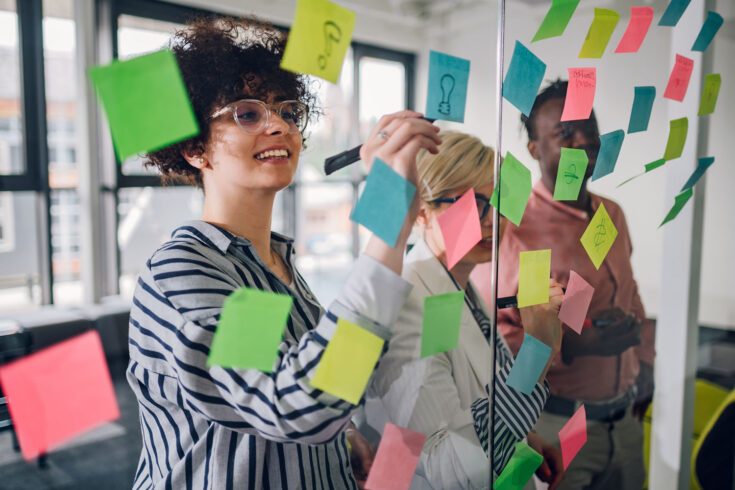 Multiracial team at work writing ideas on sticky notes on the glass wall.