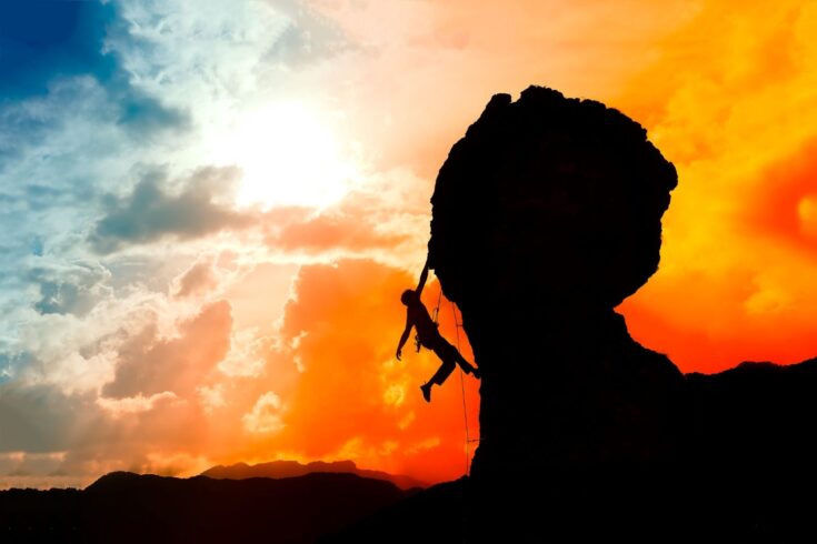 A lone climber almost at the top of the mountain reaches success at sunset with a colorful sky