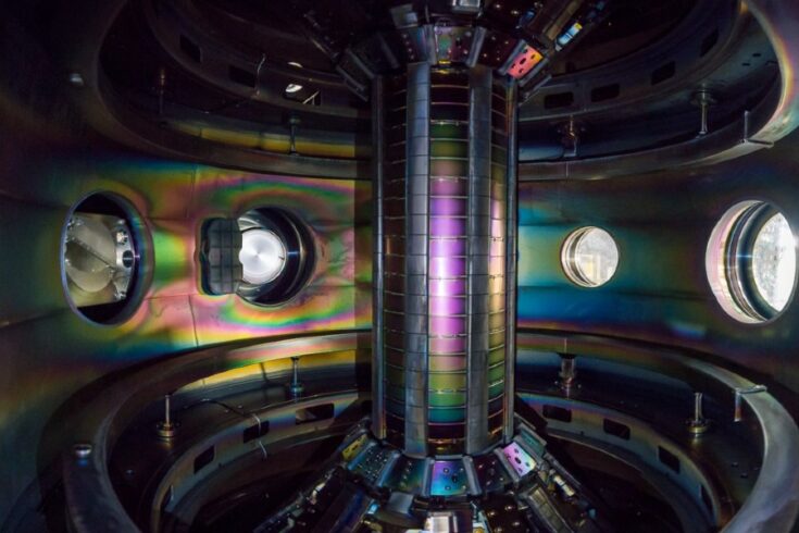 Rainbow lights shining around a metal chamber with a central column and portholes on the back wall.