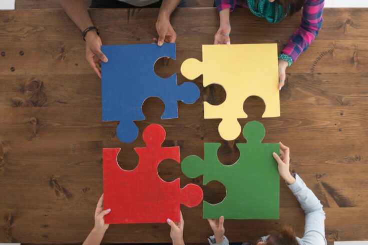 A multi-ethnic group of college age students are putting together large puzzle pieces.
